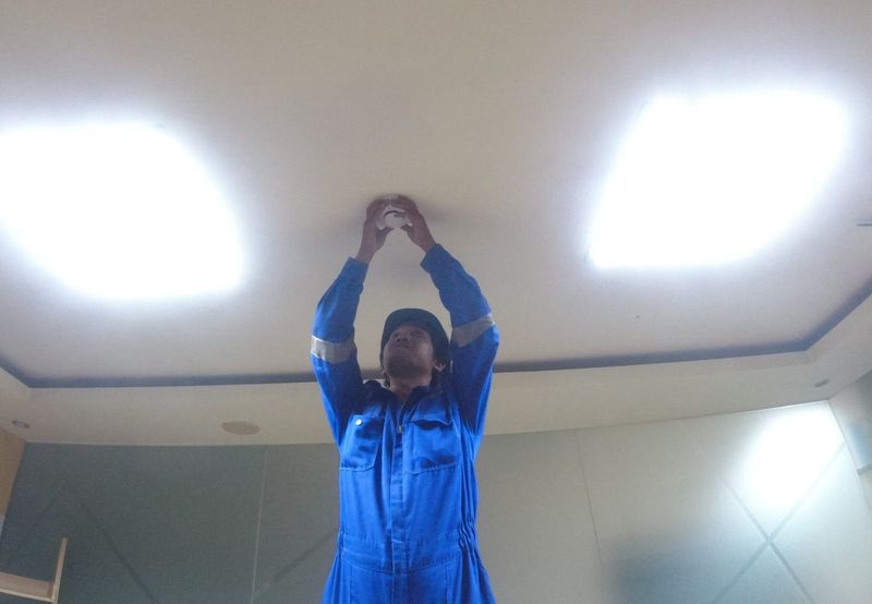 Teknisi memasang detektor asap di plafon gedung kantor