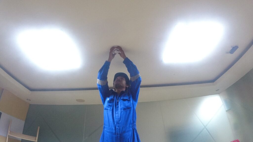Teknisi memasang smoke detector di plafon gedung kantor